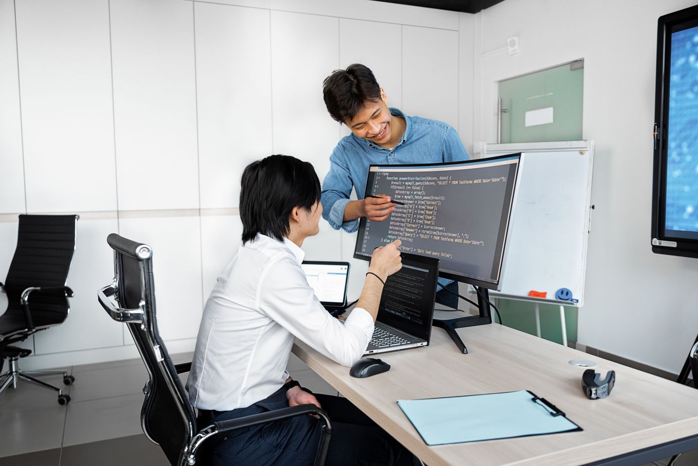 Two developers collaborating at a desk with laptops and monitors